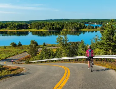 Guest cycling down road, large lake or river in background.