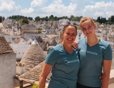 Two guests posing in front of wide shot of Alberobello.
