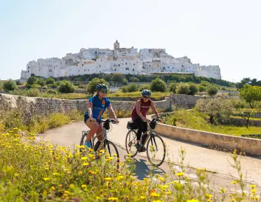 Two guests cycling in front of Ostuni hilltop.