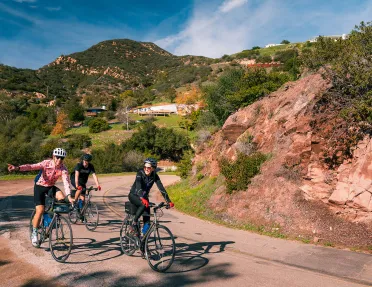 Three guests rounding corner, one pointing towards camera, Cali hills in background.