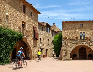 Two guests cycling through village, tan stone buildings all around.