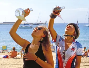 Two guests on beach, drinking from ornate wine glasses.