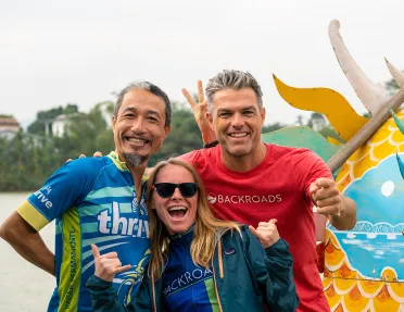 Three Backroads guests smiling and posing in front of a dragon boat in Vietnam