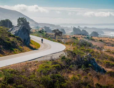 Coastal California vista, ocean and cliffs in background, cyclist in foreground.