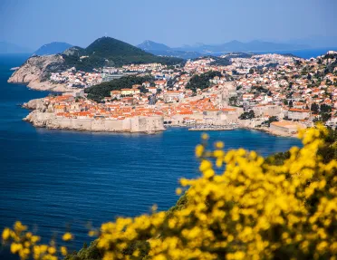 Wide shot of Dubrovnik coastline, blue ocean, white and tan houses.
