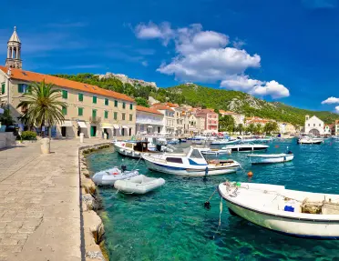 Wide shot of Croatian coastal town, boats, blue water, hills, etc.