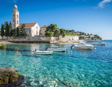 Wide shot of Hvar Island, white stone buildings, blue water, boats.