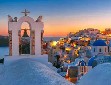 Sunset shot of Santorini, city lit up, church bell in foreground.