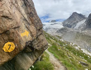 Painted trail marker on side of cliff, hiking trail in distance.