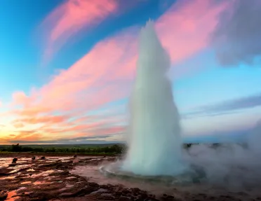 Shot of thermal geyser erupting, vibrant pink/blue sunset.