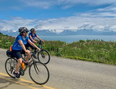 Two guests on road, cycling next to large lake. 