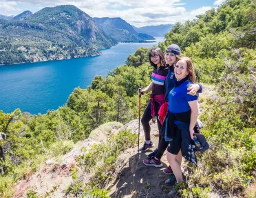Three young guests posing together, overlooking large lake, hillside.