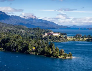 Wide shot of inlet, white building, snowy peak, larger lake in distance.