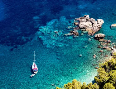 Bird's eye shot of rocky beach, small boat, blue water.
