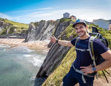 Leader gesturing to craggy cliffs, large beach, buildings dotting cliffside.