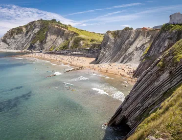 Shot of craggy cliffs, large, crowded beach in distance. 