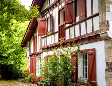 Housefront shot of red and white cottage among forest.