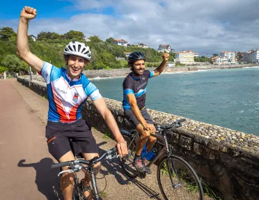 Two guests, cycling with fists raised, ocean to left.