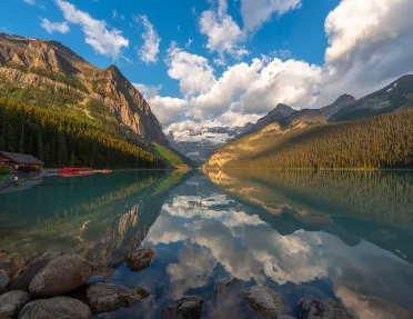 Wide shot of lake, wooden shack, mountain range, valley.