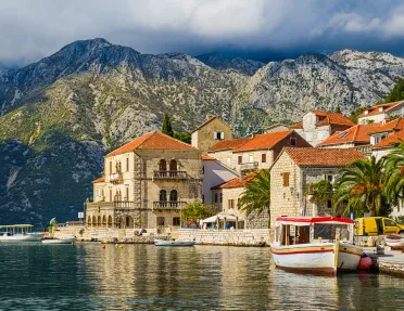 Shot of Croatian houses on coast, boats, mountain in distance.