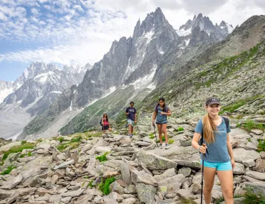 Four guests walking up craggy hillside, large, spiked mountains behind them.