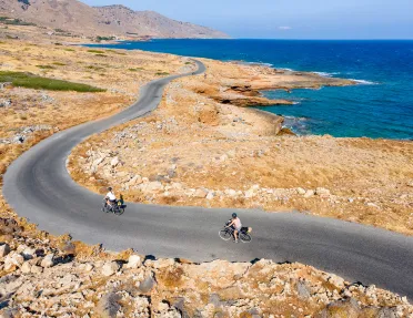 Two guests cycling along golden coastline, ocean to their right.