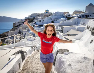 Guest emoting to camera, white walled coastal buildings behind her.