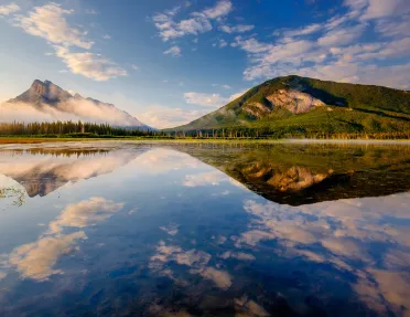 Wide shot of reflective lake, mountains during sunset.