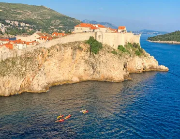 Wide shot of walled cliffside houses, guests kayaking below.