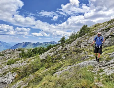 Guest hiking on craggy hillside, cloudy sky behind them.