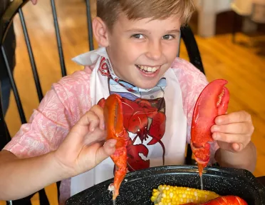 Young guest eating lobster, holding up both claws.