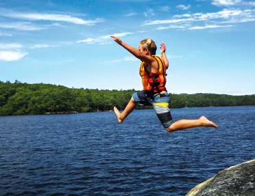 Young guest jumping from rock into lake.