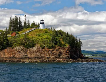 Wide shot of small island, white lighthouse and small red building on it.