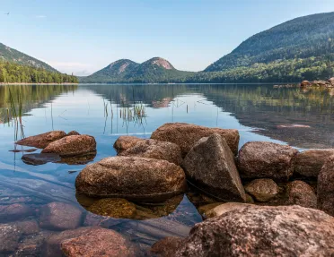 Wide shot of reflective lake, rounded mountains.