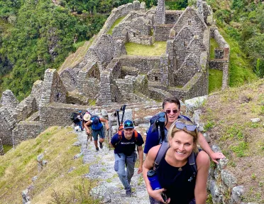 Guests hiking up stone trail, Machu Picchu ruins behind them.