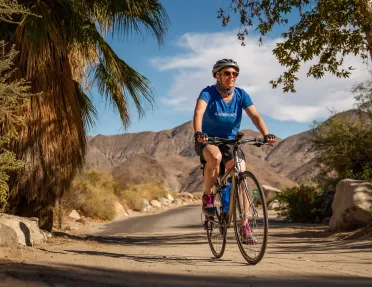 Guest cycling past palm tree, desert landscape behind him.