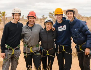 Group of five smiling for camera, all in climbing harnesses.