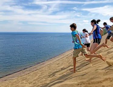 Group of young guests running down sand dune towards ocean.