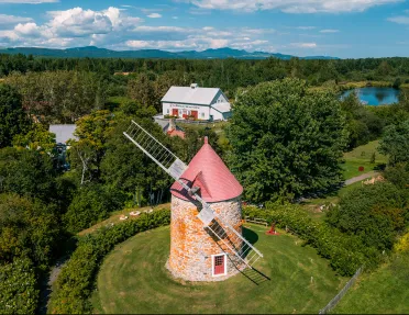 Wide shot of large windmill, white building in background.