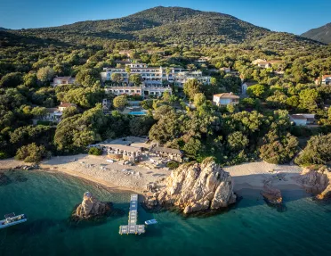 Wide shot of a large hotel in the hillside, beach, small boats and ocean in foreground.