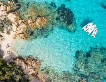Overhead shot of guests on the beach, some are on small boats in the water.