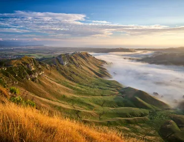 Wide shot of cloud covered valley during sunset, sloping cliffs rising from it.