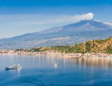 Wide shot of Mount Etna, small boats in water in foreground.