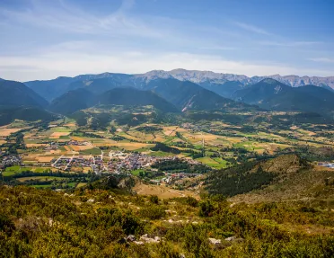 Bird's eye shot of mountainous valley, town, golden fields below.