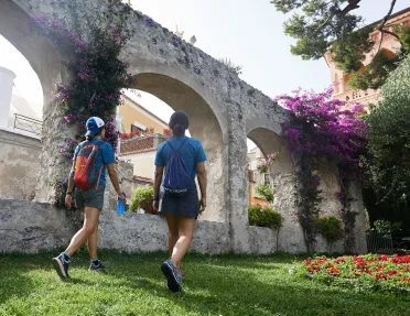 Two guests walking through arched garden. Red and purple flowers.