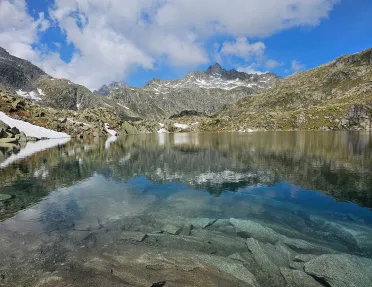 Shot of still lake, craggy rocks dotting lakeside, mountain in distance.