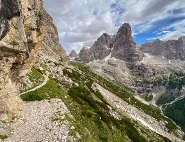 Wide shot of craggy cliffs, trails, valley, mountain in distance.