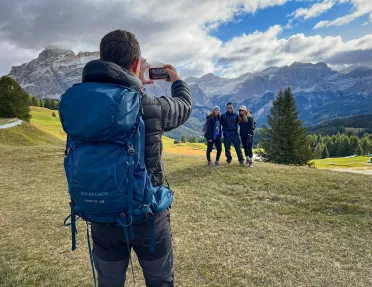 One guest taking photo of other three, mountains behind them.