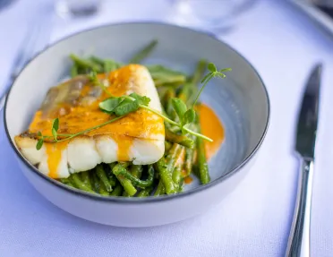 Plate of pan fried fish with an orange sauce, bed of greens.