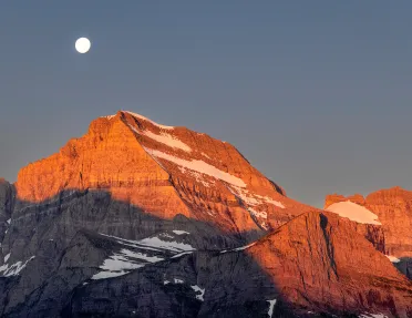Orange sunset painted onto mountain landscape and moon peering through